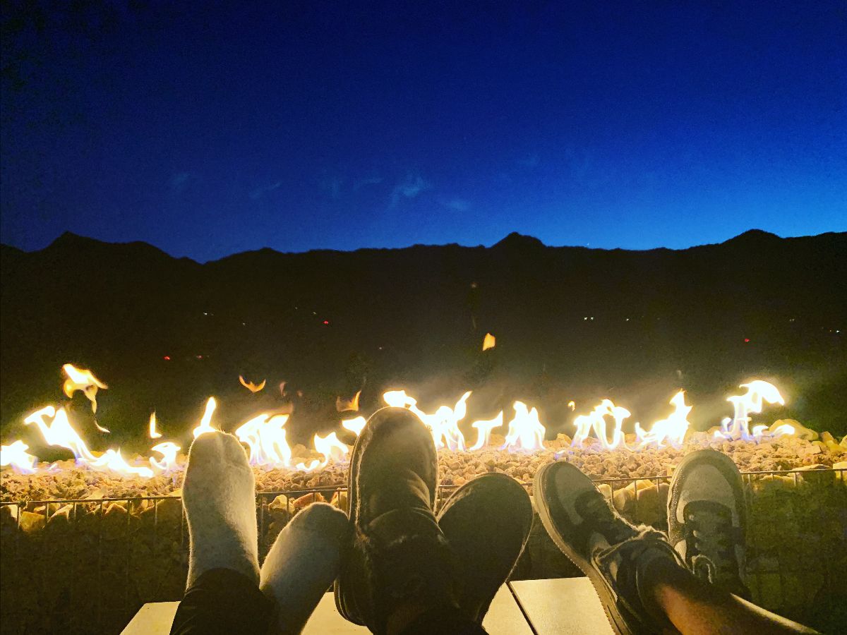 feet in front of a campfire in the desert with a striking night sky above in a deep blue
