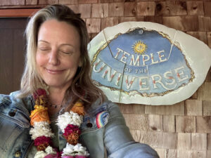 Elizabeth Winkler wearing a lei in front of a Temple of the Universe sign