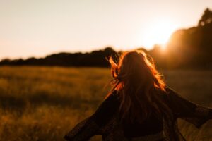 Woman freely running through grass during sun set feeling free