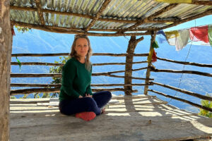 Elizabeth Winkler sitting cross legged in a hut in Bhutan with flags blowing in the wind