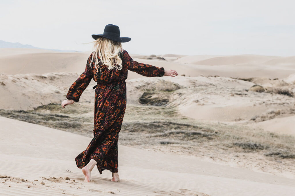 woman with hat and long flower dress dancing in the sand on the beach